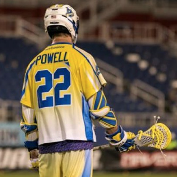 A lacrosse player wearing yellow and blue is standing on the field.